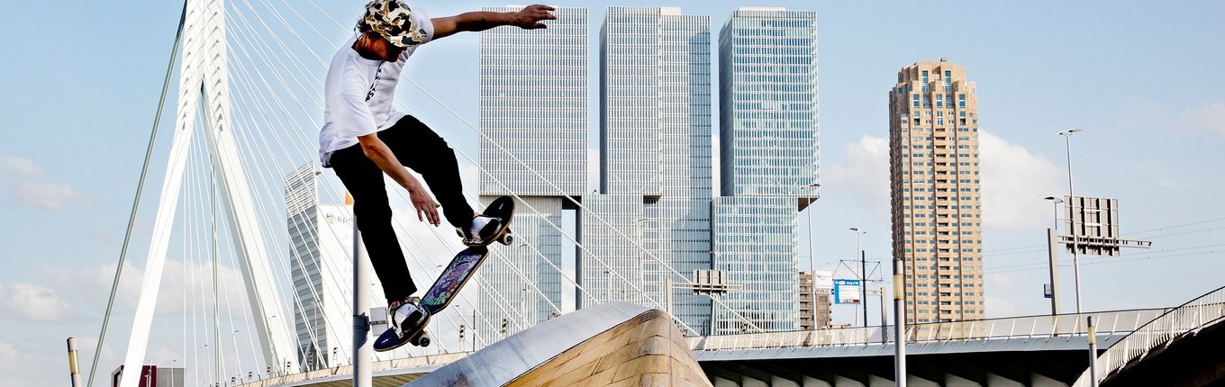 Skateboarder makes move with Rotterdam skyline background Skateboarder makes move with Rotterdam skyline background