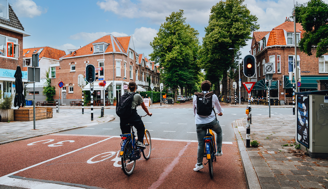 Bij een stads kruispunt wachten twee mensen op OV fietsen tot hun licht groen wordt.